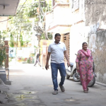 A still from a video. The still shows two people walking down a street.